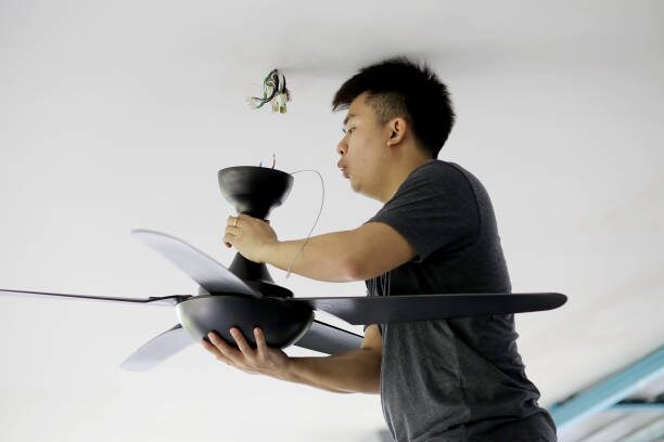 A man installing a ceiling fan in a room and wondering about the blue wire
