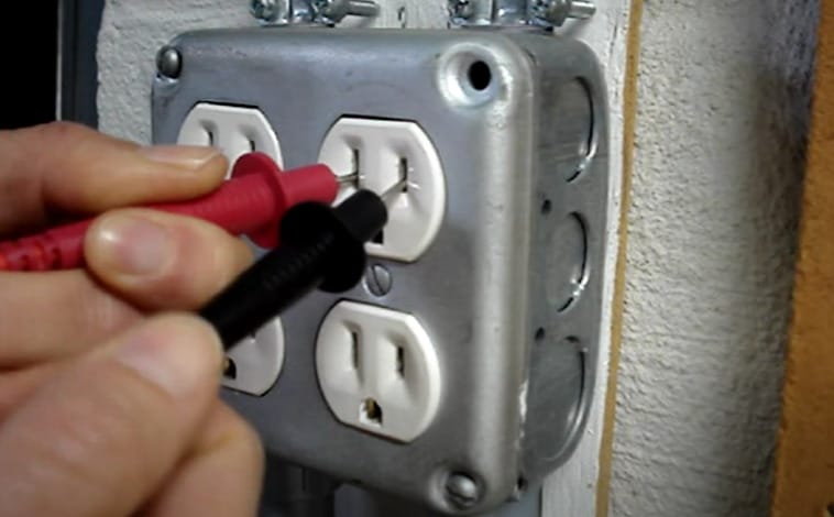 A person is using a multimeter to test an electrical outlet
