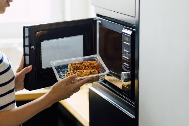 A woman is putting food into a microwave