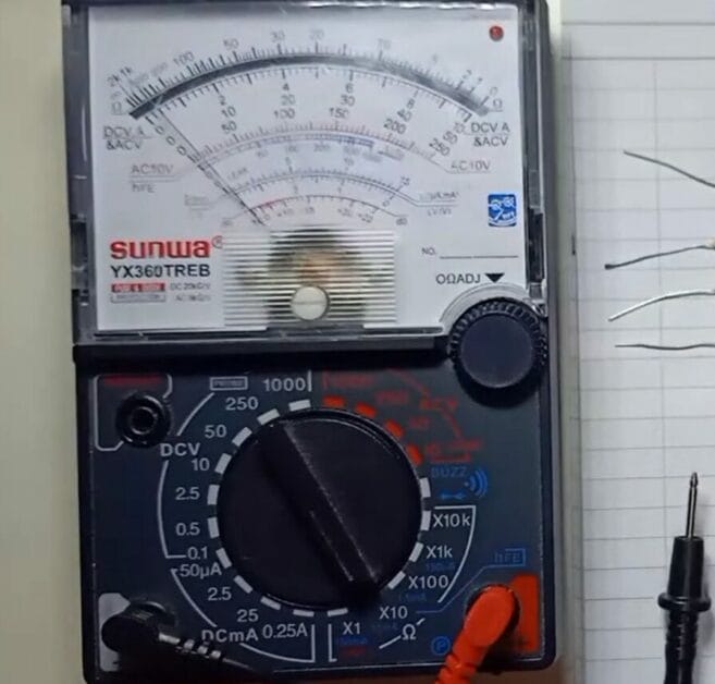A multimeter is next to a wire and a paper