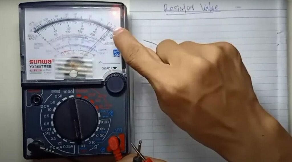 A person is holding a multimeter in front of a notebook, measuring resistance