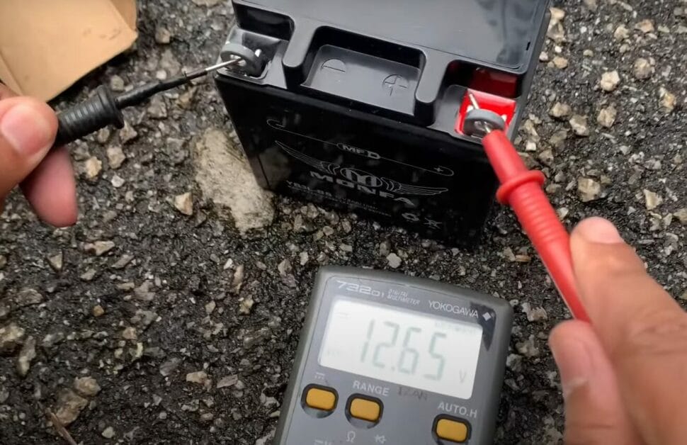 A person is using a multimeter to test a 12v battery