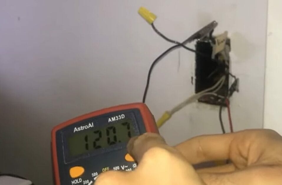 A person using a multimeter to test a wall outlet wires