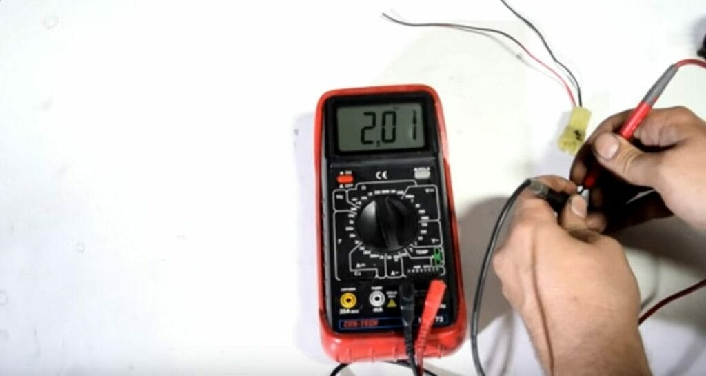 A person touching the multimeter’s leads to the sensor’s terminal pins