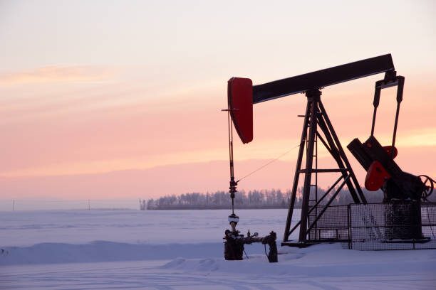 An oil pump in the snow at sunset, tirelessly drilling a well