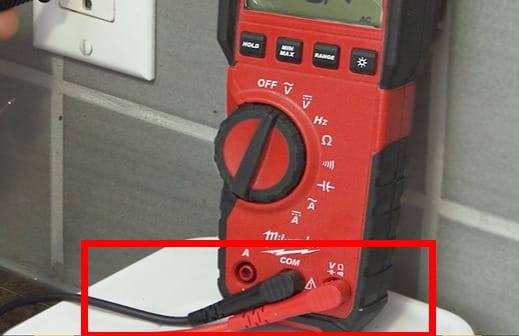 A person is attaching the multimeter probe to test an outlet