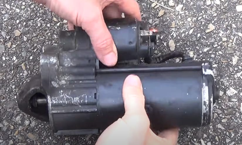 A person is holding a black starter motor on the ground