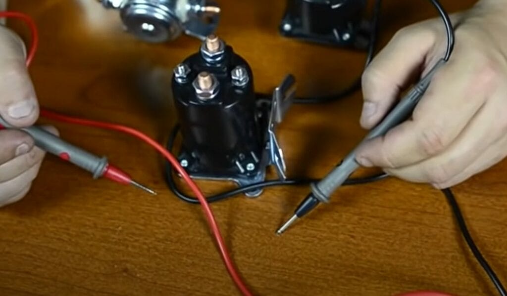 A person is working with wires on a table to test a solenoid using a multimeter