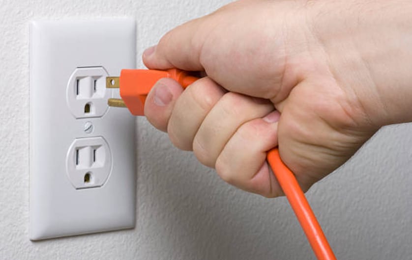 a person is plugging an orange wire into a wall outlet