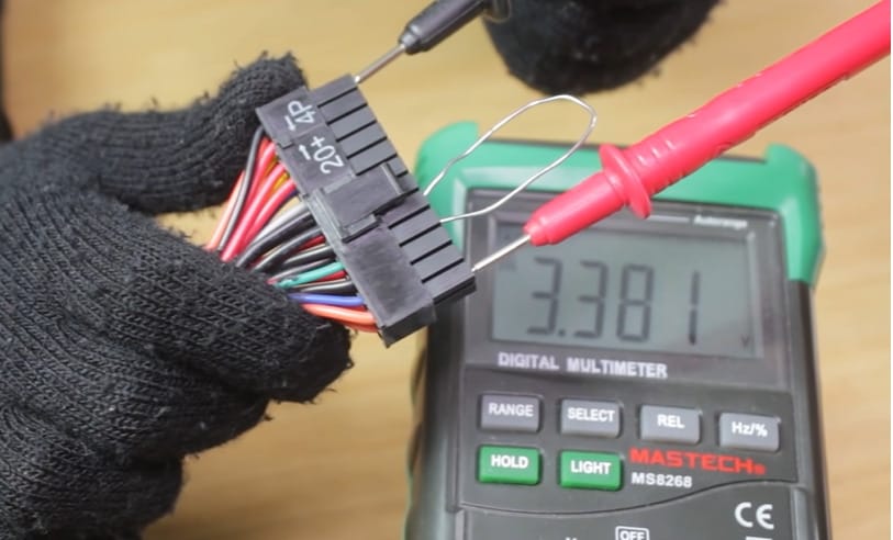 A person is using a multimeter to test a 24-pin connector of a PC power supply