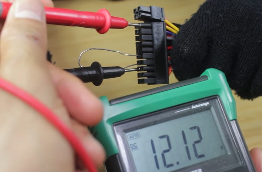A person is testing a 24-pin connector with a multimeter