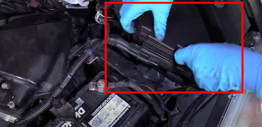A person in blue gloves is checking the fuse box of a car