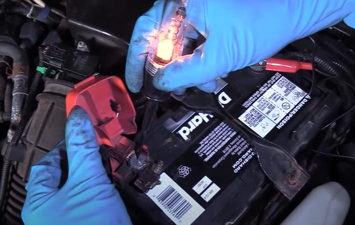 A person in a blue gloves is using a test light to check the fuses in a car battery