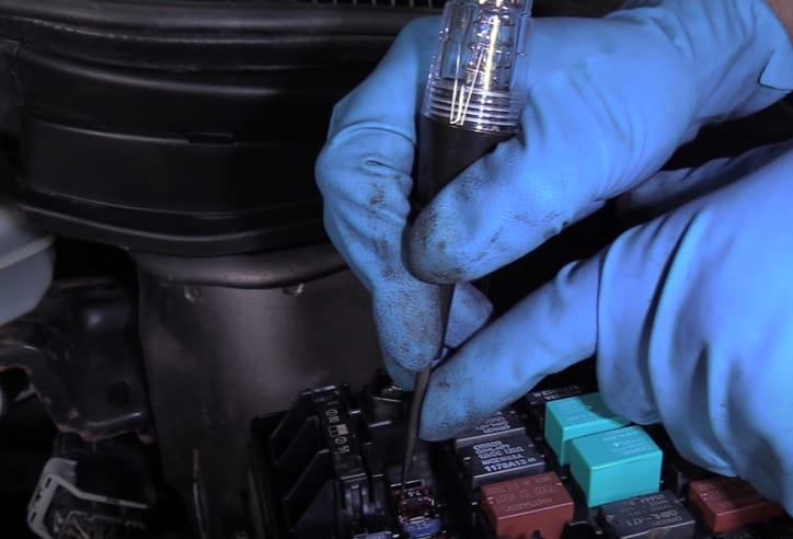 A person in blue gloves is using a test light showing no light when testing car fuses