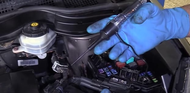 A person in blue gloves is using a test light to check fuses on a car