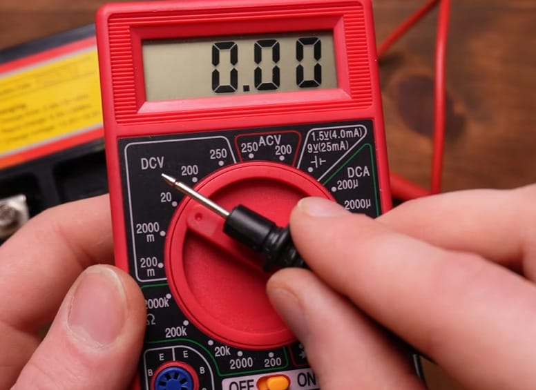 A person is holding a multimeter set at 0.00 initial reading
