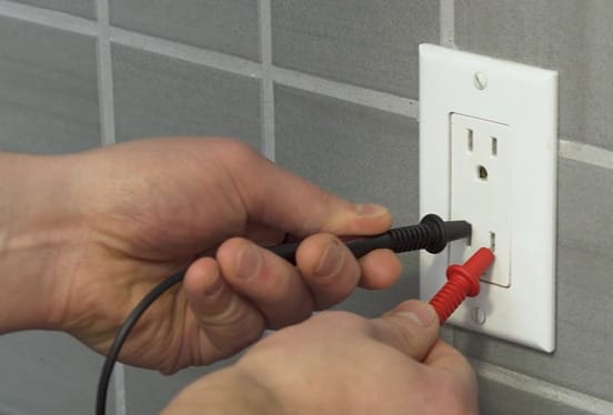 A person is using a multimeter to test an outlet