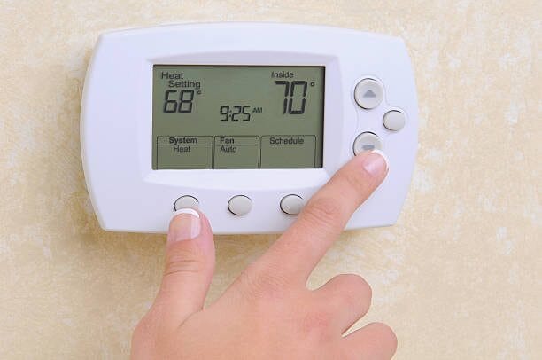 A person is pushing buttons of a thermostat on the wall