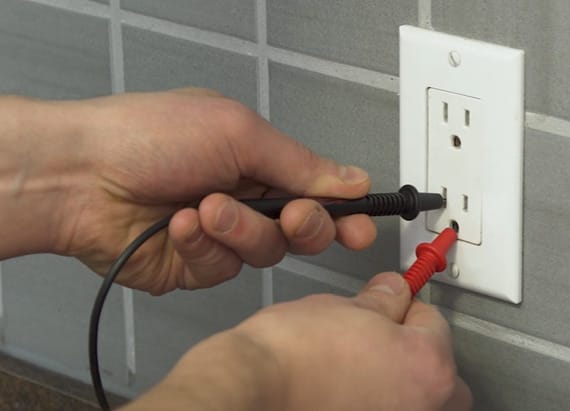 A person is inserting the multimeter probe on the outlet