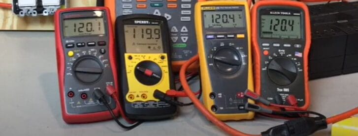 A group of different multimeters on a table, including a true RMS multimeter