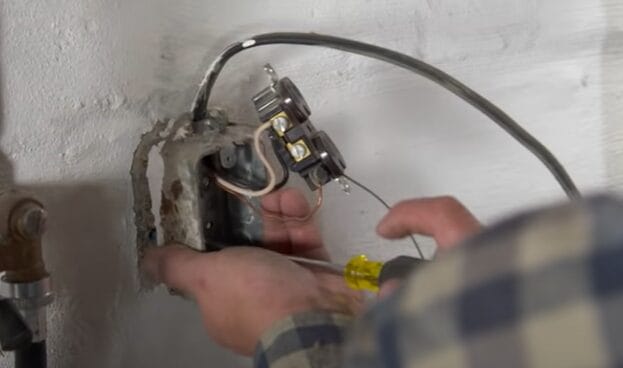 A man is using a screw to wire and install an outlet on the wall
