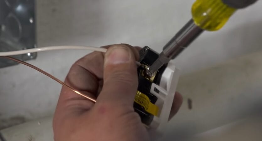 A person is using a screwdriver to fix an outlet wiring