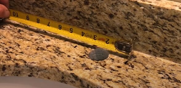 A person measuring a sink with a measuring tape to determine the exact dimensions for drilling a hole in their granite countertop