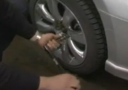 A man using a breaker bar to fix a tire on a silver car
