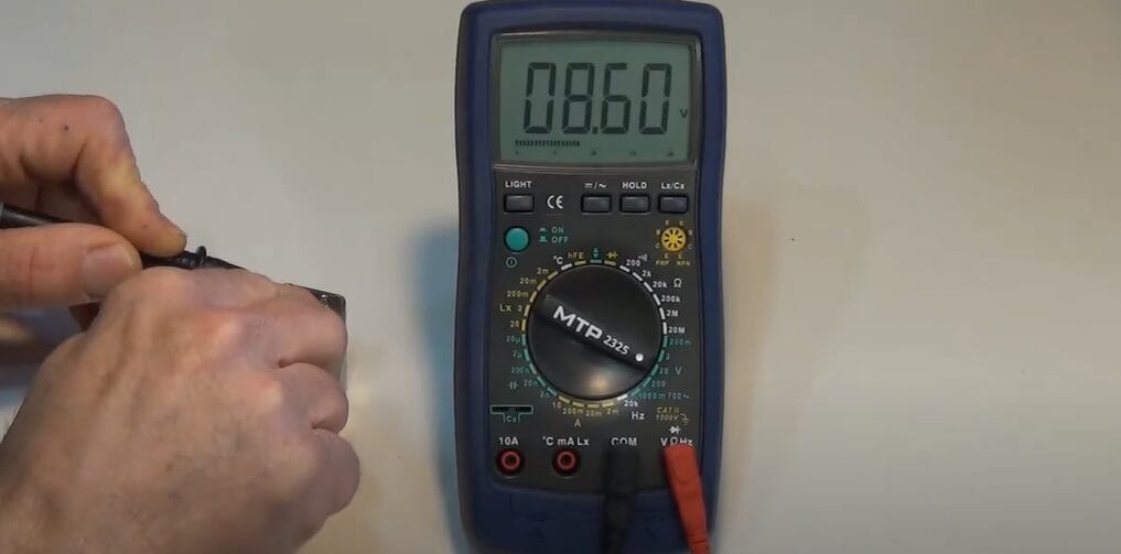 A person using a multimeter to measure the DC voltage of a wire