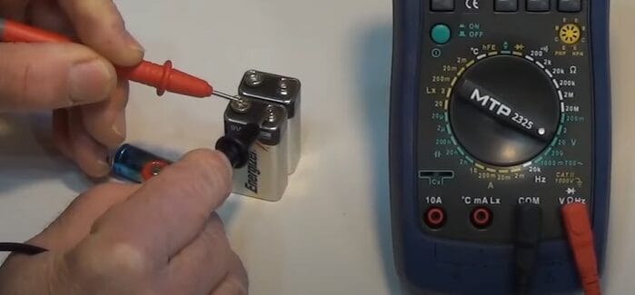A person is using a multimeter to measure DC voltage of a battery
