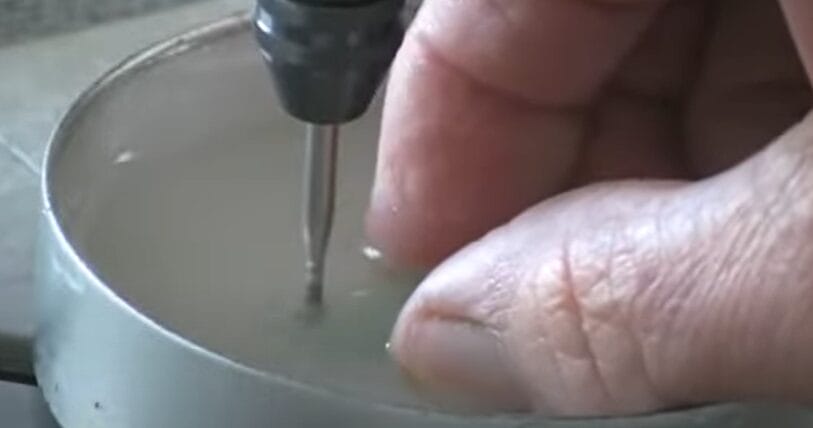 A person is using a screwdriver to drill a hole in sea glass