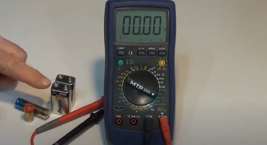 A person using a multimeter to measure the DC voltage of a battery