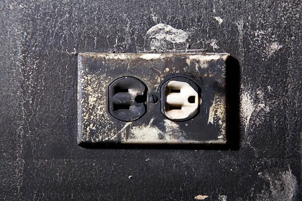 A black and white electrical outlet with rust on it emitting a faint electrical burning smell