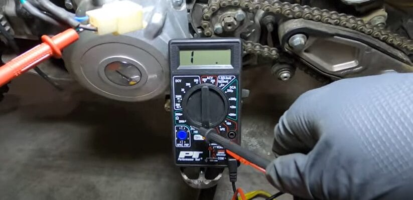A person is using a multimeter to test a motorcycle stator