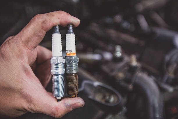 A person holding two spark plugs in front of a car