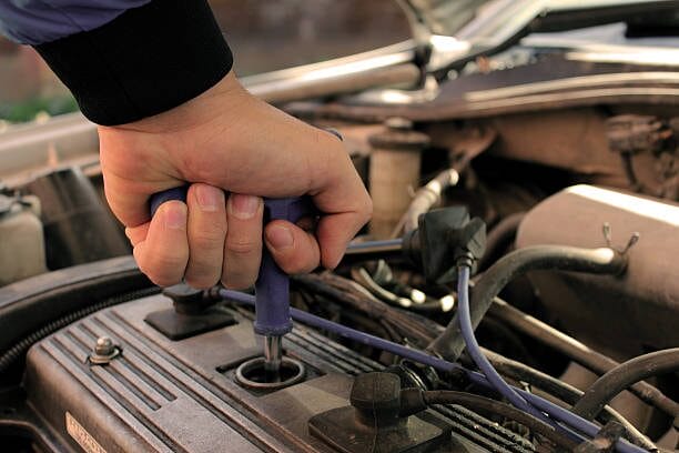 A man is working on the engine of a car, checking the spark plug wires durability