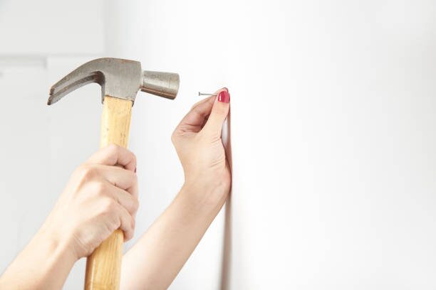 A woman holding hammering a nail on a white wall