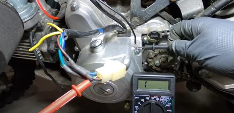 A person is using a multimeter to test the stator on a motorcycle