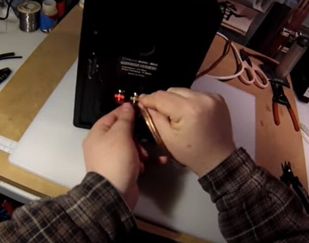 A person is putting a speaker wire into a black box and learning how to strip it