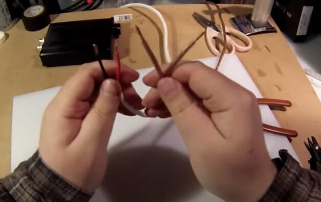A person is holding two wires together on a table while demonstrating how to strip speaker wire