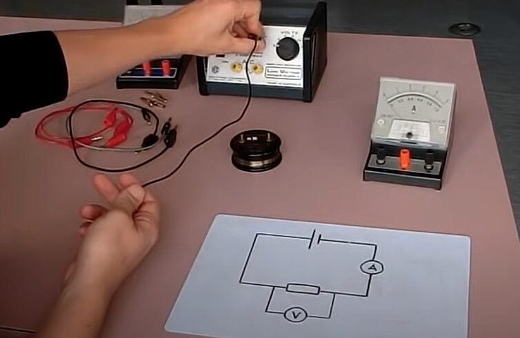 A person is working with an electronic device connecting an ammeter to a circuit on a table