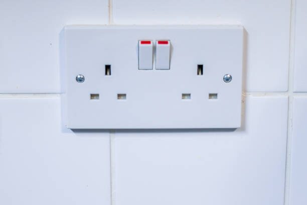 A white power socket on a tiled wall that allows you to check 240 voltage with a multimeter