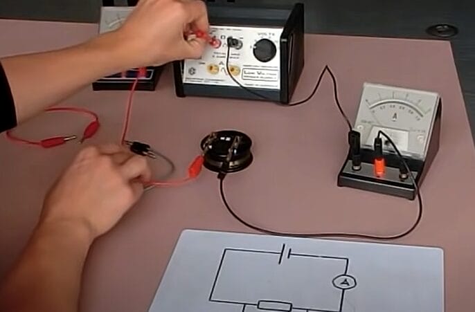 A person is working with an electronic device on a table, connecting an ammeter to a circuit