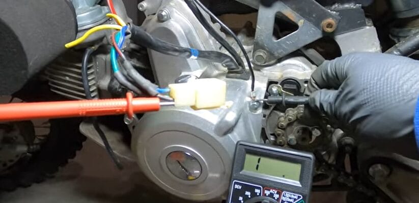 A person is testing a motorcycle stator using a multimeter