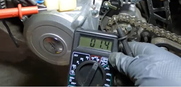 A person testing the stator of a motorcycle using a multimeter