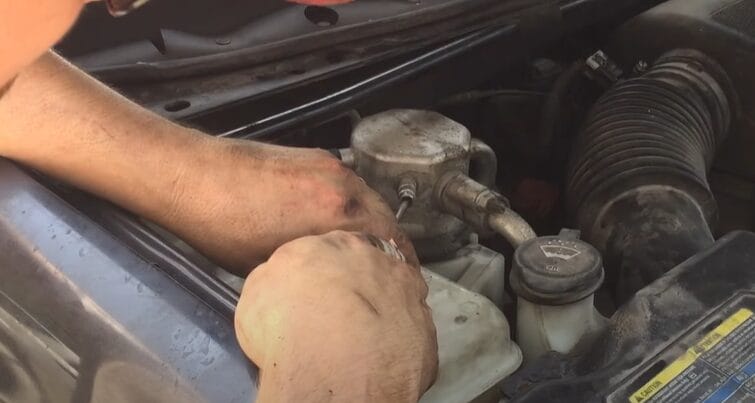 A man is working on the engine of a car, figuring out how to jump a 3-wire AC pressure switch