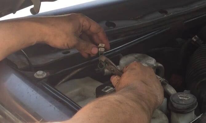 A man is working on the engine of a car, troubleshooting the wiring of a 3-wire AC pressure switch