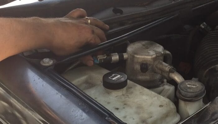 A man is working on the hood of a car, figuring out how to jump the 3-wire AC pressure switch