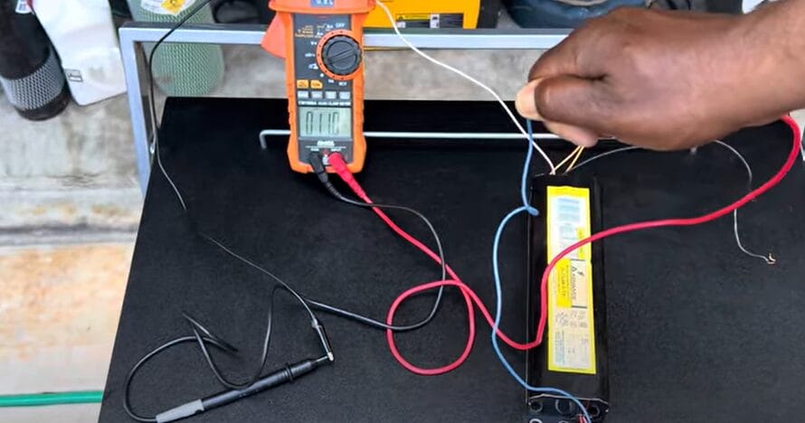 A person using a multimeter to test a wire on a table by following the steps to test a ballast