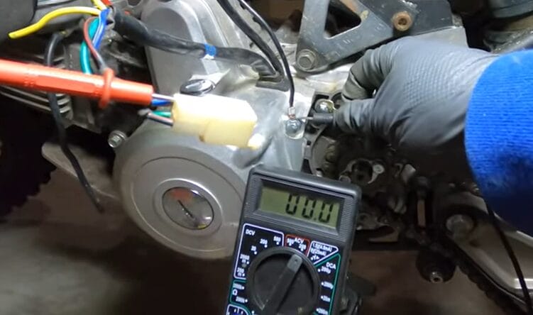 A person is testing a motorcycle's stator using a multimeter